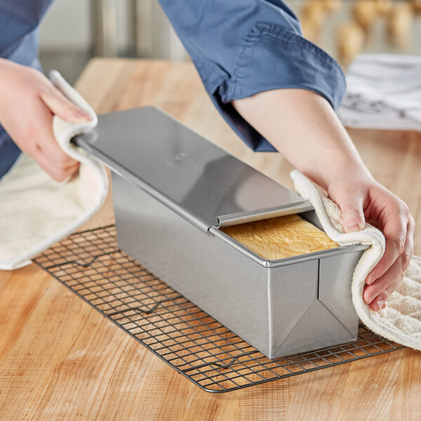 A person using a Chicago Metallic aluminized steel loaf pan with a cover to bake bread.