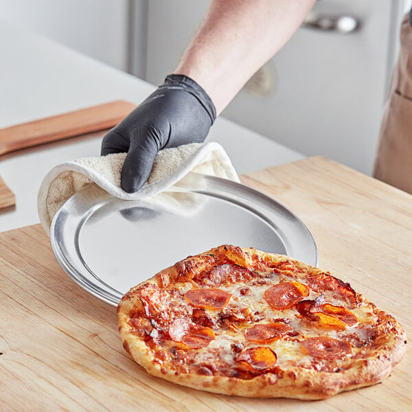 A gloved hand holding a pepperoni pizza on a Choice aluminum pizza pan.