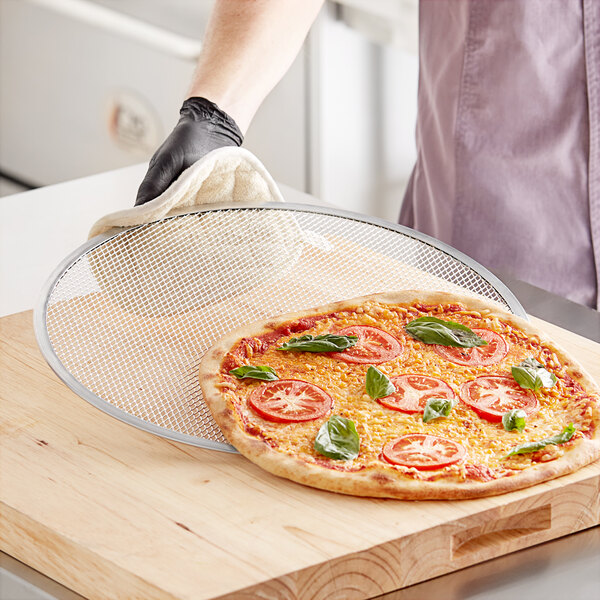 A person wearing black gloves uses a white cloth to hold a pizza on a cutting board.