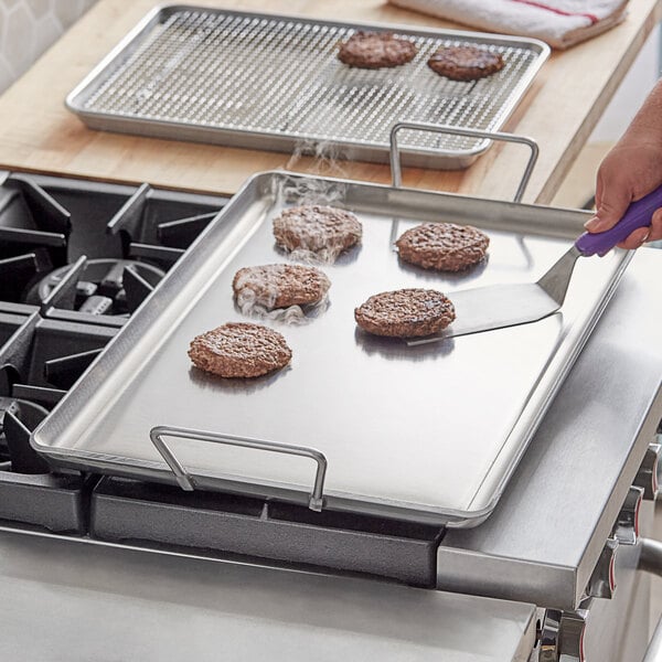 A person cooking hamburgers on a Vigor portable aluminum griddle on a stove top.