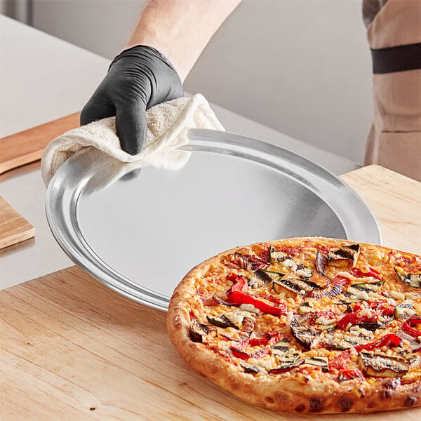 A hand in a black glove holding a Choice aluminum pizza pan with a pizza on it.