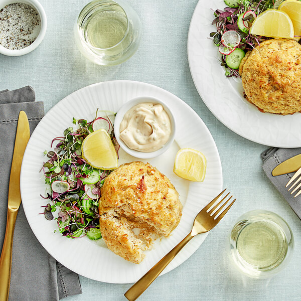 A plate with a Chesapeake Crab Connection blue crab cake, lemons, and a side of white sauce.