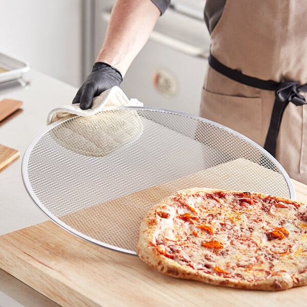 A person holding a pizza on a Choice aluminum pizza screen.