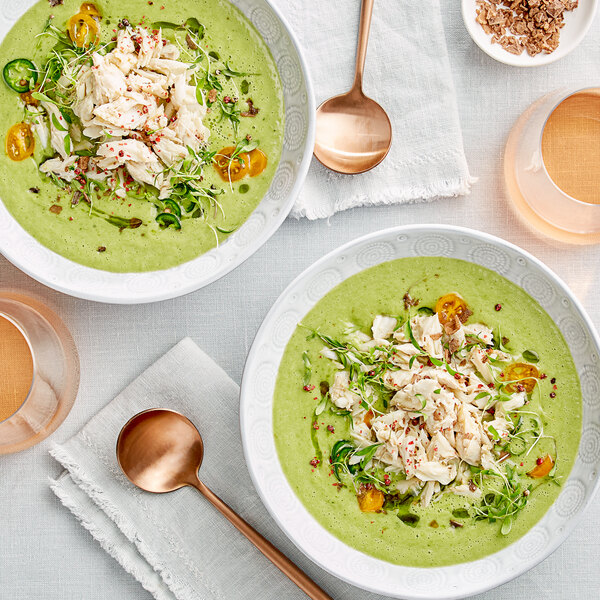 A group of bowls of green soup with Chesapeake crab meat and vegetables next to a spoon.
