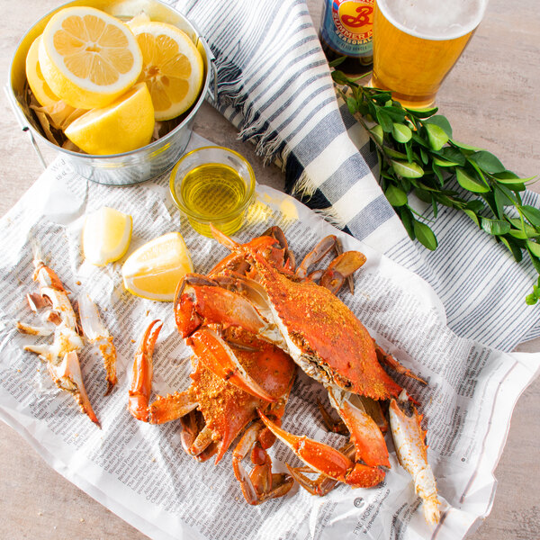 A steamed blue crab on a newspaper with lemon slices and a bowl of beer.