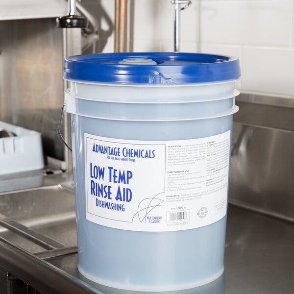 A 5 gallon bucket of Advantage Chemicals low temperature rinse aid sitting on a counter.