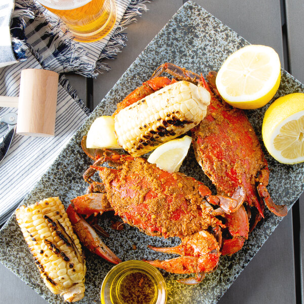 A plate of Chesapeake blue crabs with corn and lemon wedges on a table.