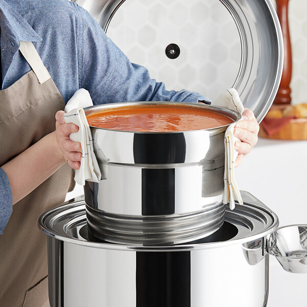 A person using an Acopa Voyage round chafer food pan to hold a large pot of soup.