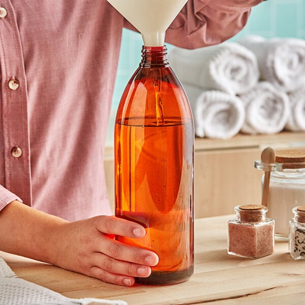 A hand pouring liquid into a 32 oz. amber Bullet Cosmo PET bottle.