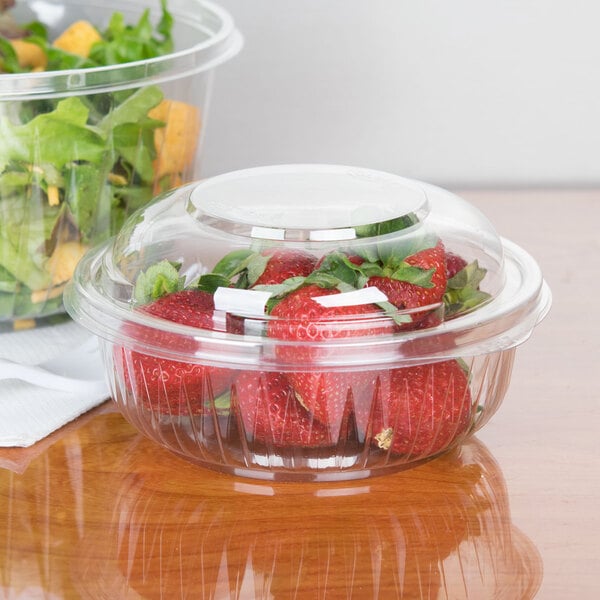 A Dart clear plastic bowl with strawberries and a salad in it.