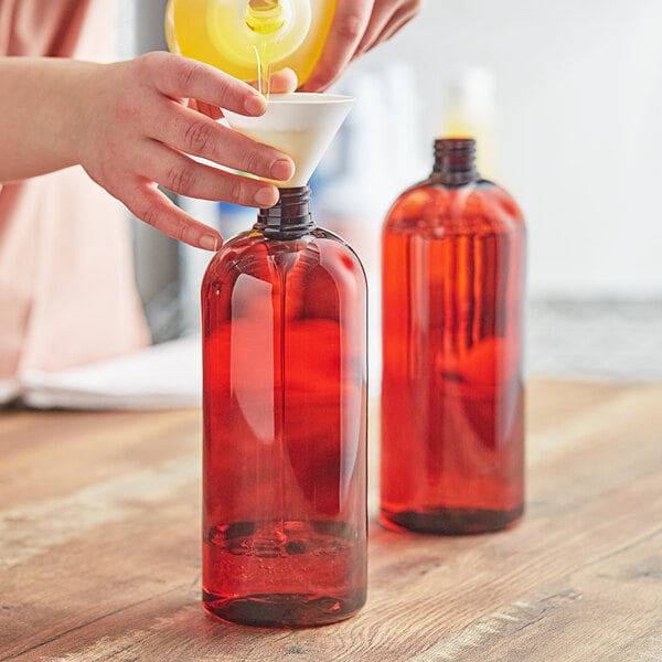 A person pouring red liquid into a 32 oz. Boston Round PET Amber Bottle.