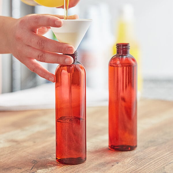 A person pouring liquid into an 8 oz. amber Bullet Cosmo PET bottle.