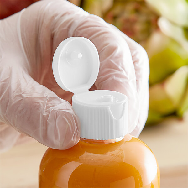 A hand holding a 24/410 white plastic flip top lid on a plastic bottle of orange juice.
