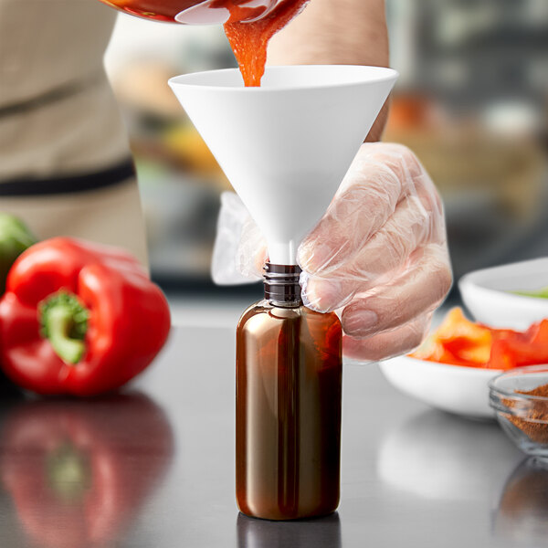 A hand pouring sauce into a 4 oz. amber bottle using a funnel.