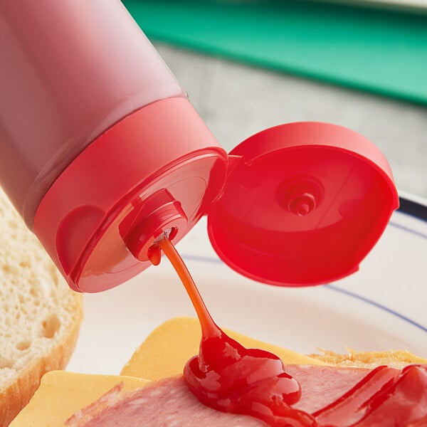 A 38/400 red squeeze bottle lid with pressure sensitive liner on a bottle of ketchup being poured onto a sandwich.