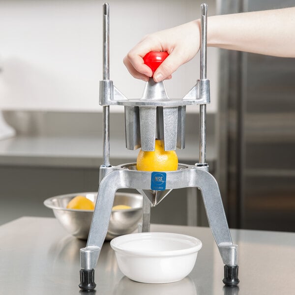 A person using a Vollrath Wedgemaster to cut a lemon into wedges over a white bowl.