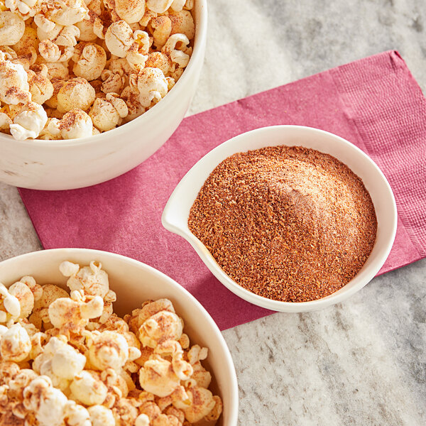A bowl of popcorn and a bowl of brown powder seasoning on a table.