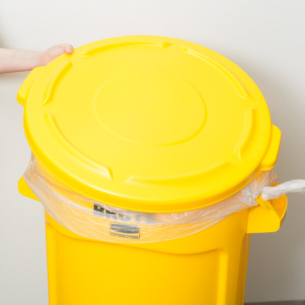 A person's hand placing a yellow Rubbermaid trash can lid over a yellow Rubbermaid trash can.