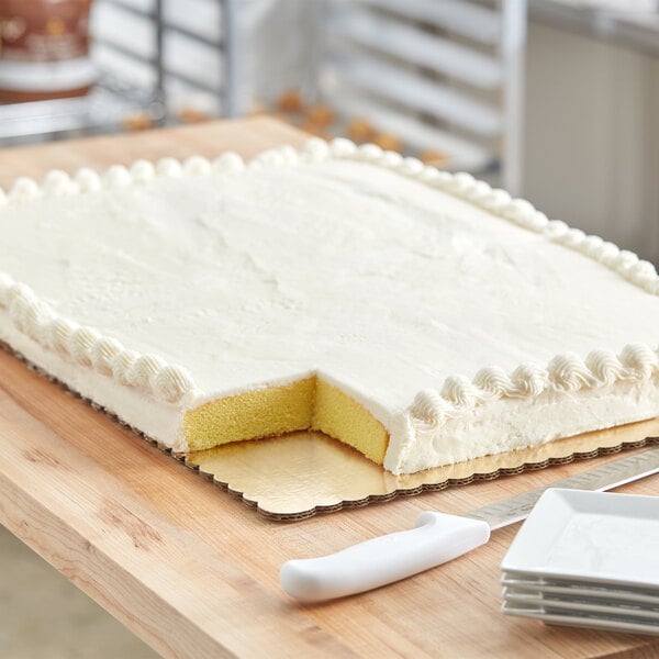 A cake with white frosting on a gold laminated corrugated full sheet cake board with a slice missing.