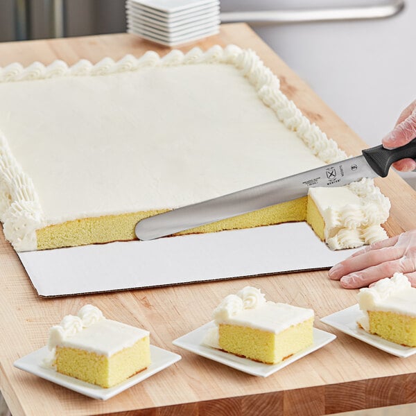 A person using a knife to cut white frosted cake on a white corrugated cake pad.