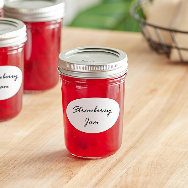 A jar of strawberry jam with an oval Avery label on a table.