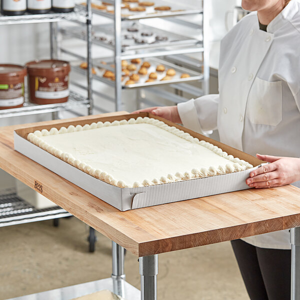 A woman holding a white corrugated bakery tray with a large white rectangular cake.