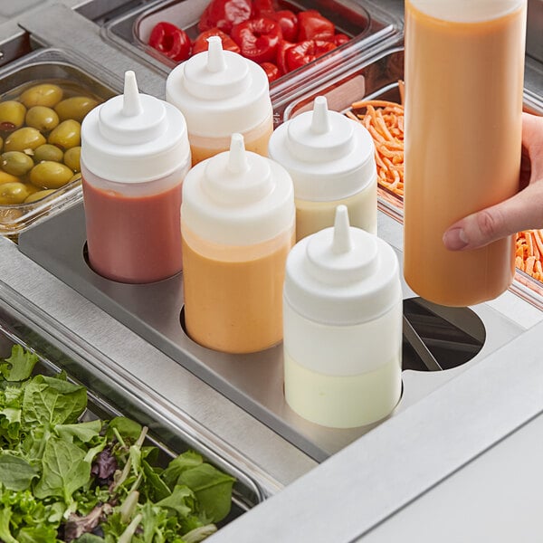 A person using a Choice stainless steel squeeze bottle holder to pour red sauce into a salad container.