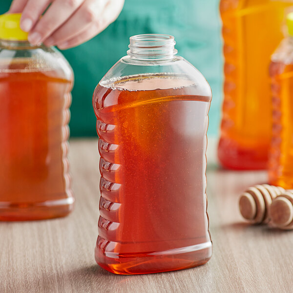 A hand pouring honey into a ribbed hourglass PET honey bottle.