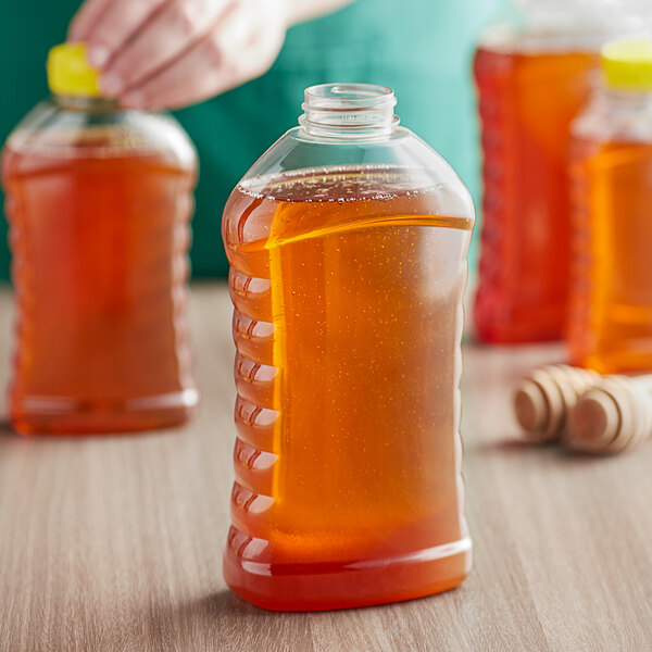 A close-up of a Ribbed Hourglass PET Honey Bottle filled with brown liquid.