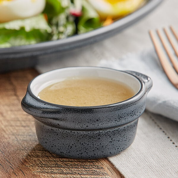 An Acopa Midnight Blue stoneware sauce cup filled with salad dressing on a table
