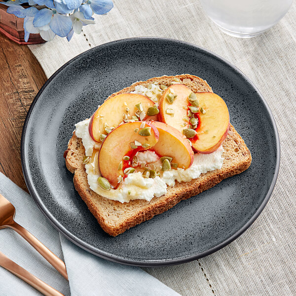 A close-up of an Acopa Embers Midnight Blue Matte Coupe Stoneware Plate with a slice of toast topped with peaches and cream