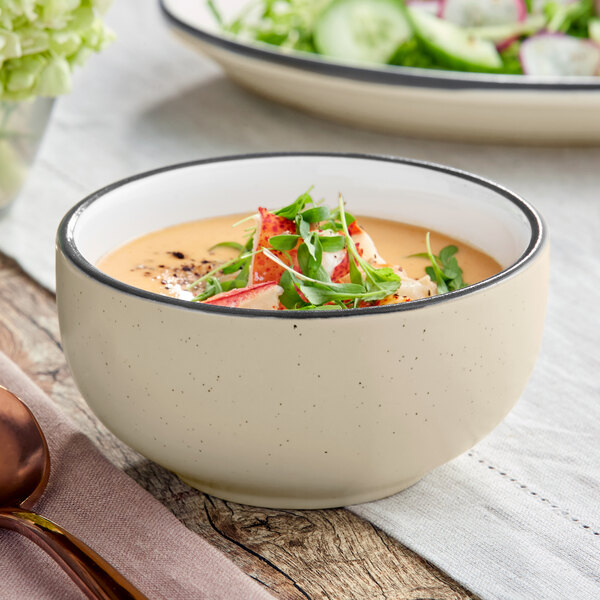 An Acopa Embers cream white stoneware bowl filled with soup and a salad on a white background.