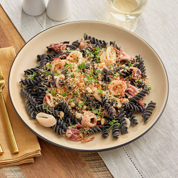 A plate of pasta with shrimp and vegetables on an Acopa Harvest Tan matte stoneware plate.