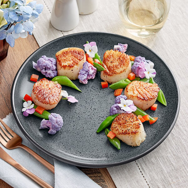 A Midnight Blue Acopa Embers stoneware plate with a seared scallop and vegetables.