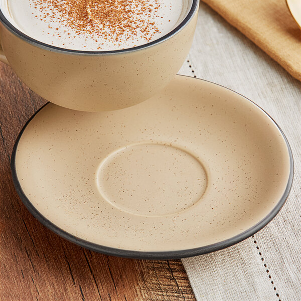 A cup of coffee with a foamy top on an Acopa Harvest Tan stoneware saucer.