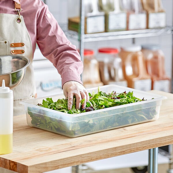 A person in an apron using a plastic container to hold greens for a salad.