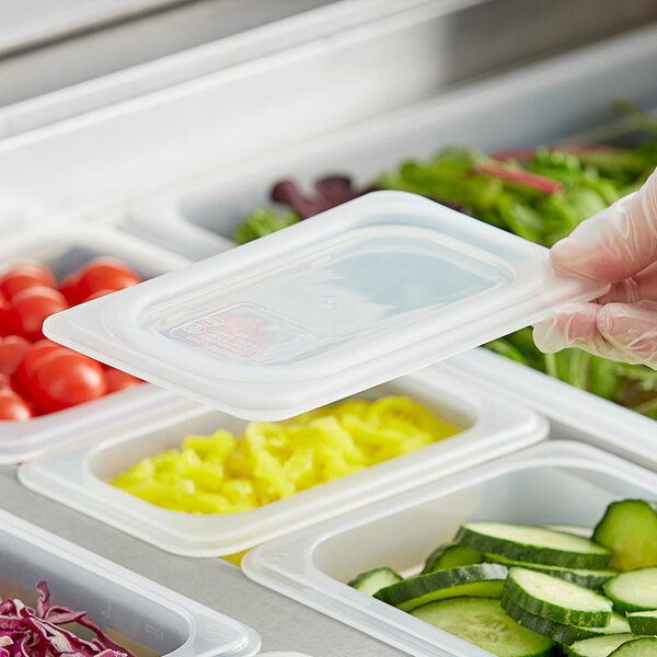 A hand in gloves securing a Vigor translucent polypropylene lid on a plastic container of cucumber slices.