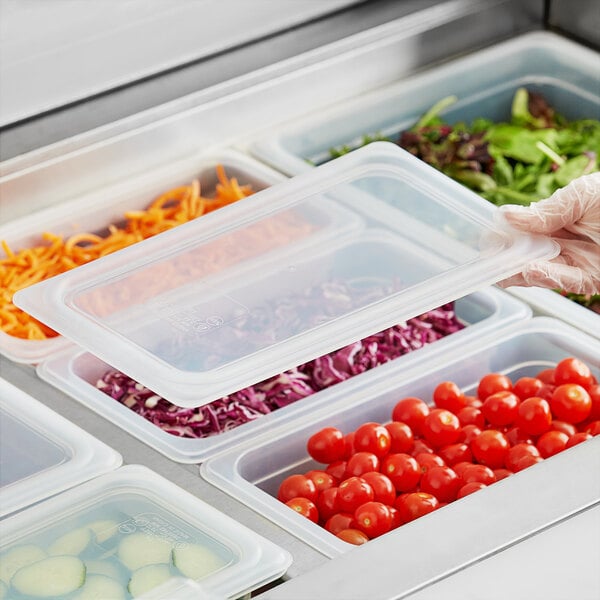 A person using a Vigor translucent plastic lid on a container of vegetables at a salad bar.