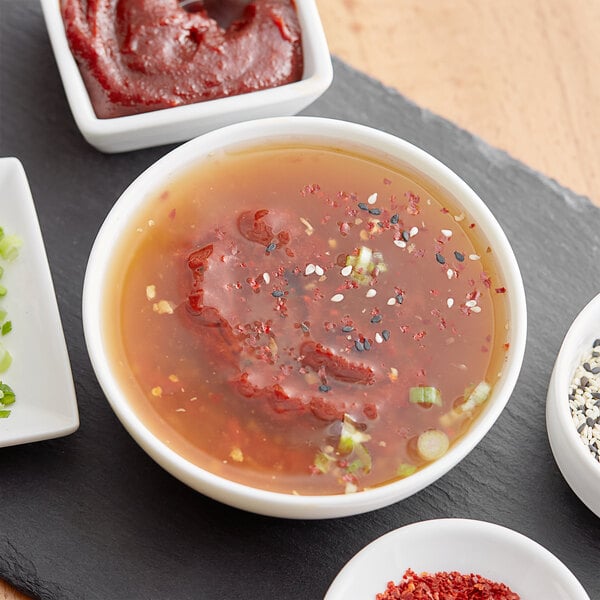 A white plate with red food on it and a bowl of soup with red hot pepper paste and green onions.
