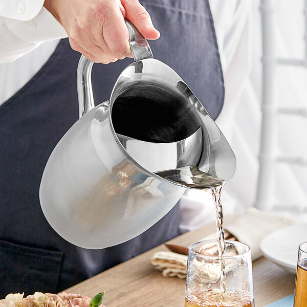 A person pouring liquid into a Tablecraft stainless steel bell pitcher.