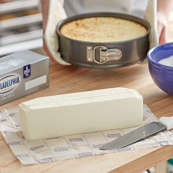 A person cutting a block of Philadelphia Original Firm Cream Cheese on a table.