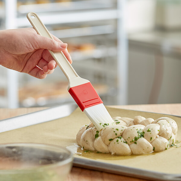 A person's hand using a white and red Choice pastry / basting brush to brush dough.