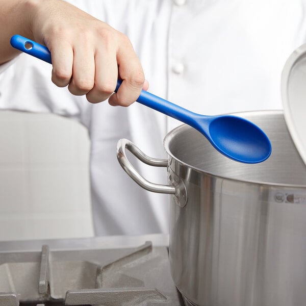 A chef using a Vollrath blue high heat nylon prep spoon to stir a pot.