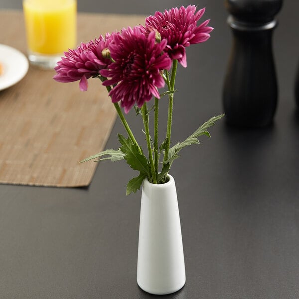 An American Metalcraft white ceramic tower vase with purple flowers on a table.