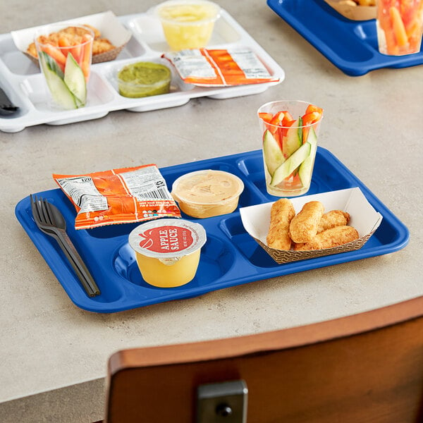 A blue Choice left-handed compartment tray with food, a yellow cup, and a glass of vegetables on a table.