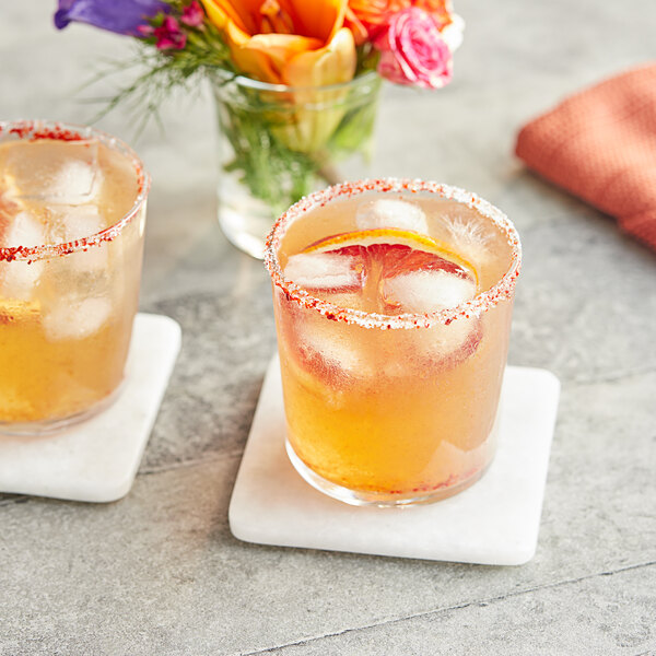 A glass of Tamarind Slab 1.1 lb. juice with ice and orange slices on a coaster with flowers.