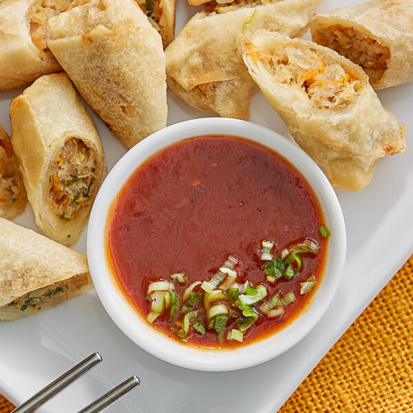 A plate of fried egg rolls with a bowl of Ashoka Tango Mango Dipping Sauce.