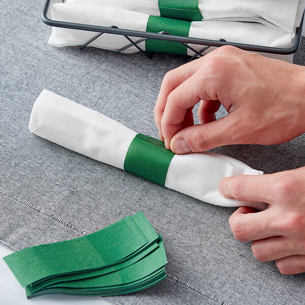 A hand using a green Hunter Green Self-Adhering Paper Napkin Band to wrap a napkin