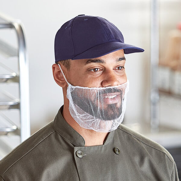 A man wearing a white nylon beard net over his beard and a blue hat.