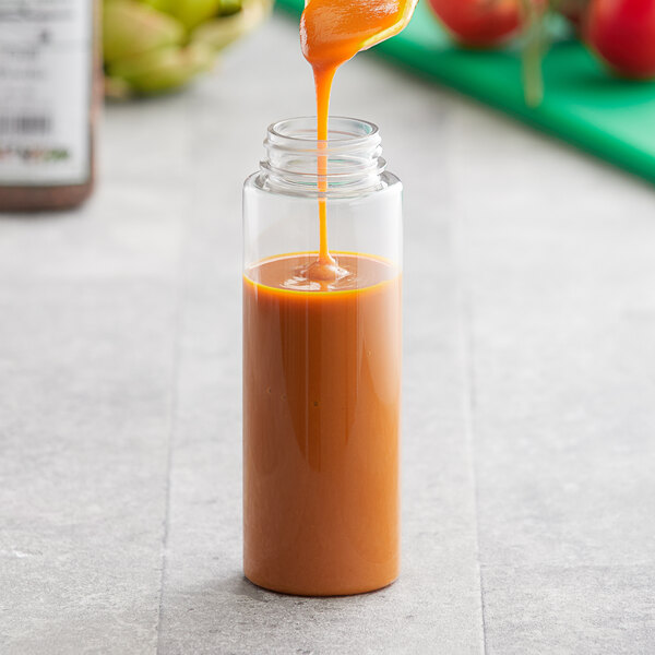 Liquid pouring from a bottle into a glass container of orange sauce.